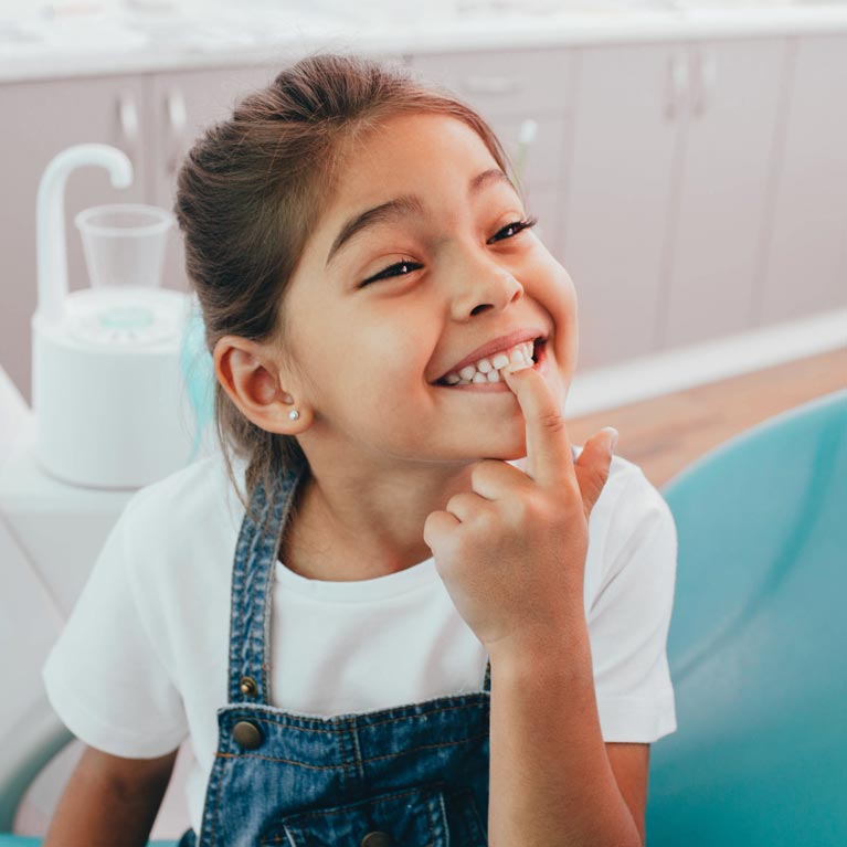 Smiling girl in dental chair pointing at her teeth